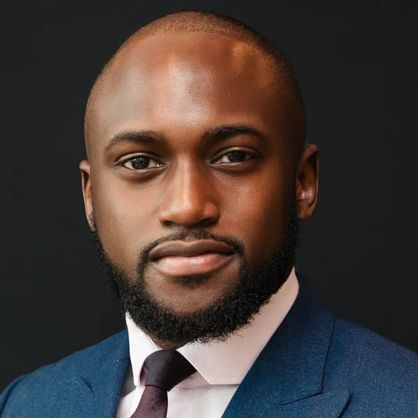 Benji Otieno, SkinBestie’s founder, in a navy double-breasted suit against a dark studio background